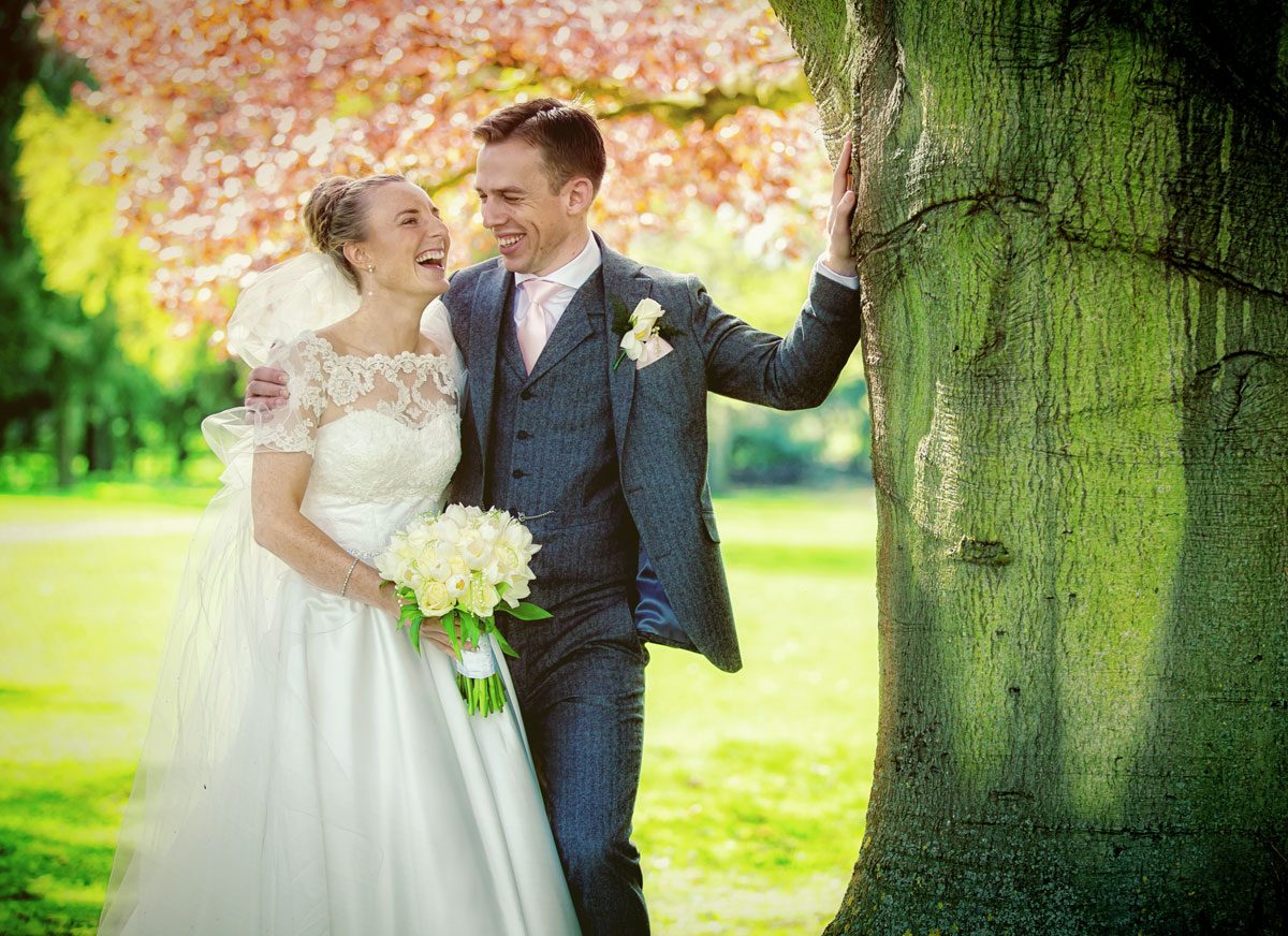 couple laugh by tree at Fanhams Hall wedding in Hertfordshire