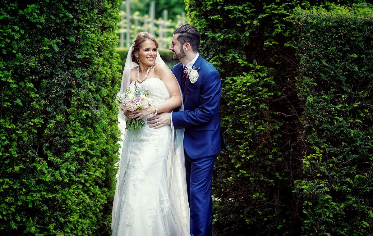 Bride and groom laugh between bushes at Fanhams Hall wedding