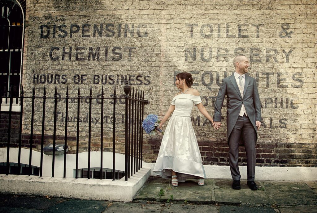 Couple hold hands by old wall for Islington Town Hall wedding photographers