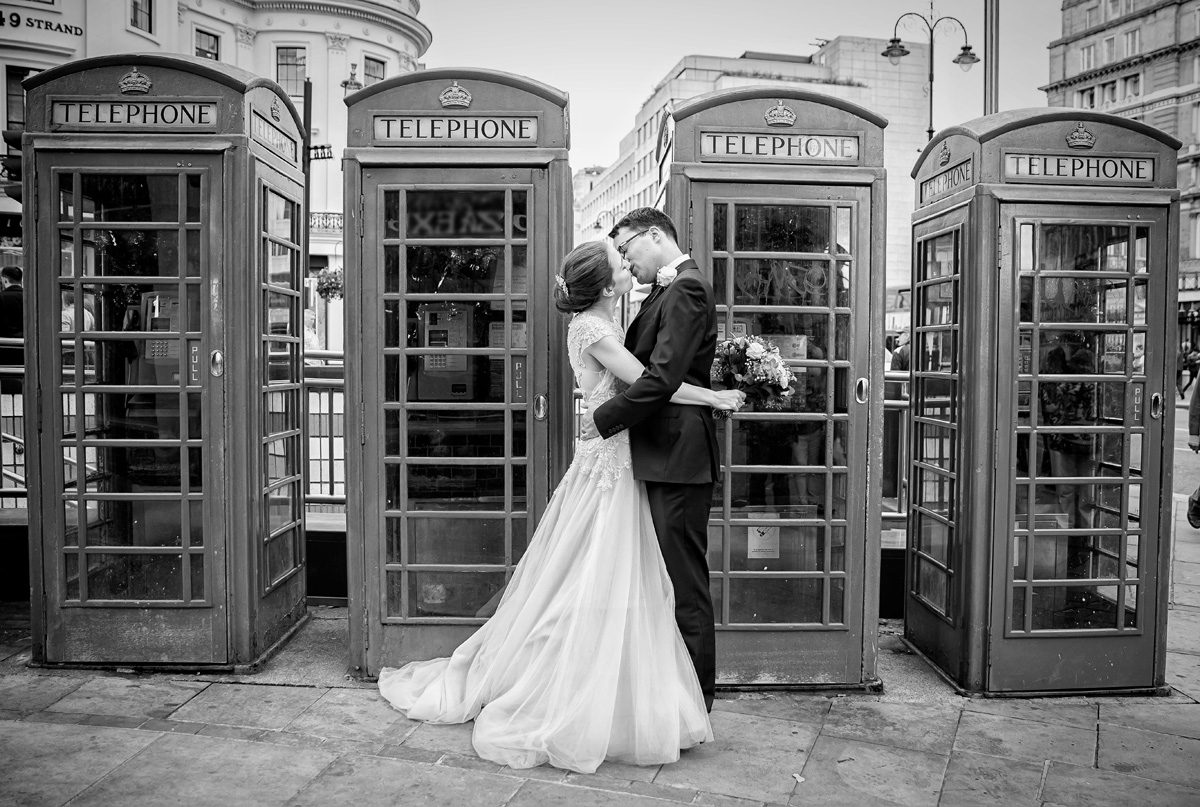 Bride and groom kiss in front of London phone boxes after wedding