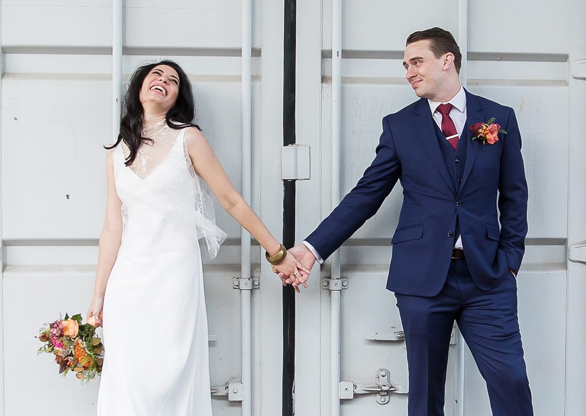 Wedding couple hold hands and laugh at Trinity Buoy Wharf