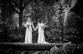 Two brides at their wedding hold hands on a bridge
