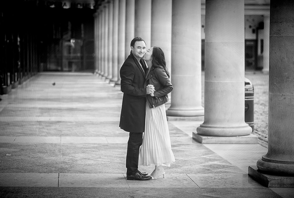 Couple kiss by pillars in Covent Garden engagement shoot