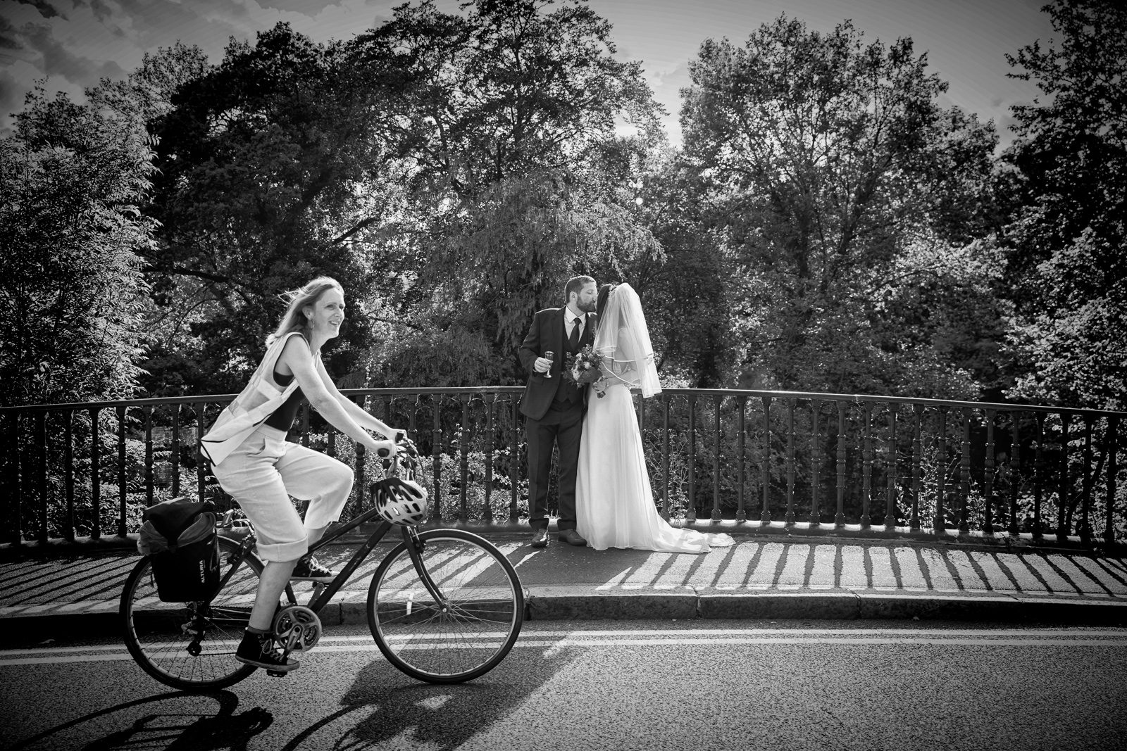 Cyclist rides past bride and groom Regents Park bridge London