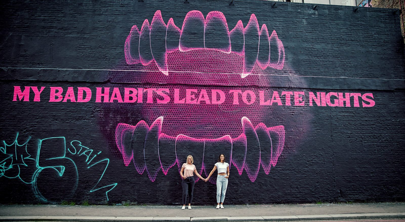 Shoreditch engagement couple in front of large graffiti on black wall London